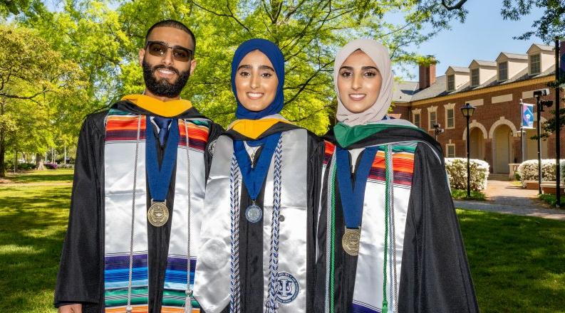 Sana, Seena and Fozi Alkaifi pose in graduation regalia with Rollins Hall in the background.